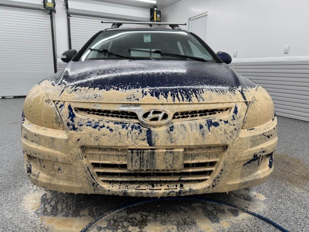 Tan Dark Fury foam covering the grille and front bumper of a dark blue Hyundai at roughly 15:1, leaving the older clear coat unmarked