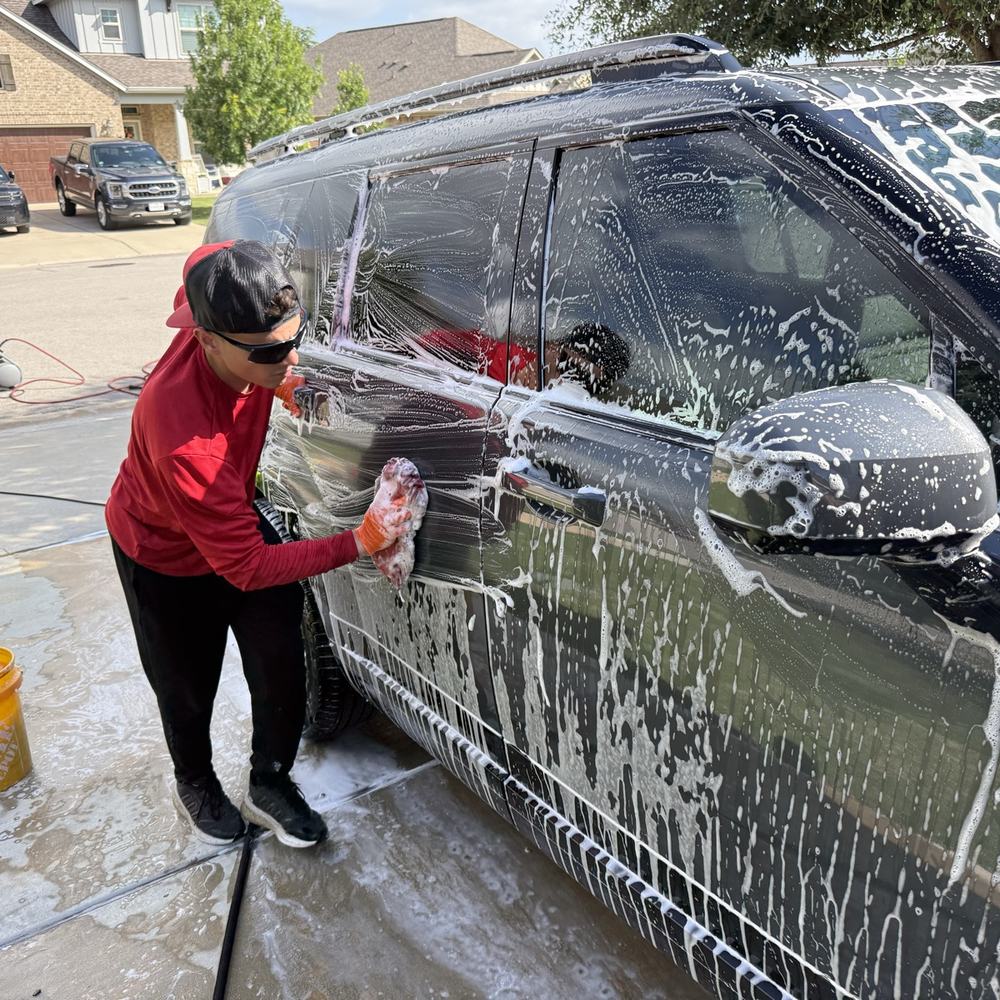 Detailer washing a Range Rover in a driveway
